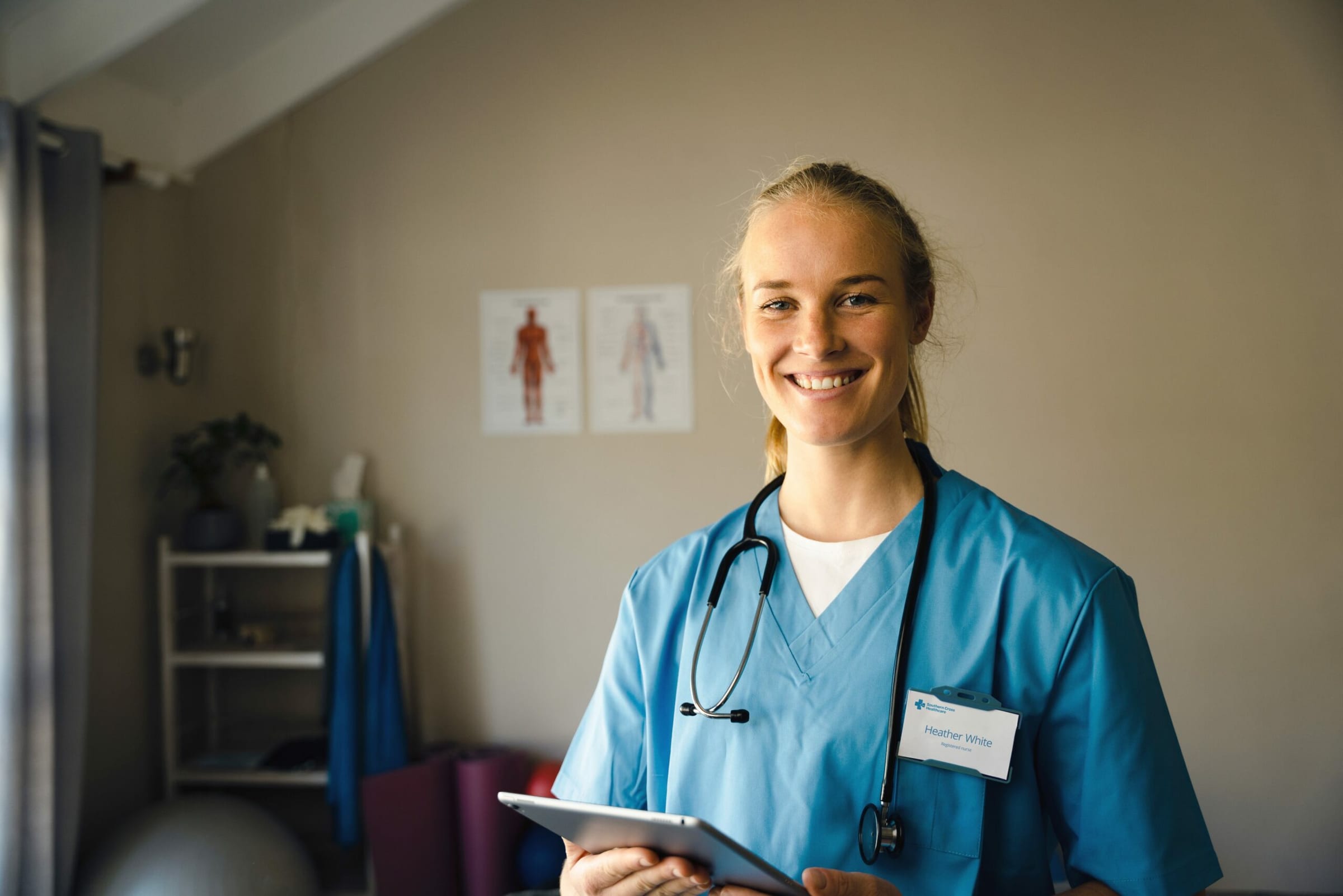 Smiling Southern Cross Healthcare nurse in blue scrubs holding a tablet, with a stethoscope around her neck