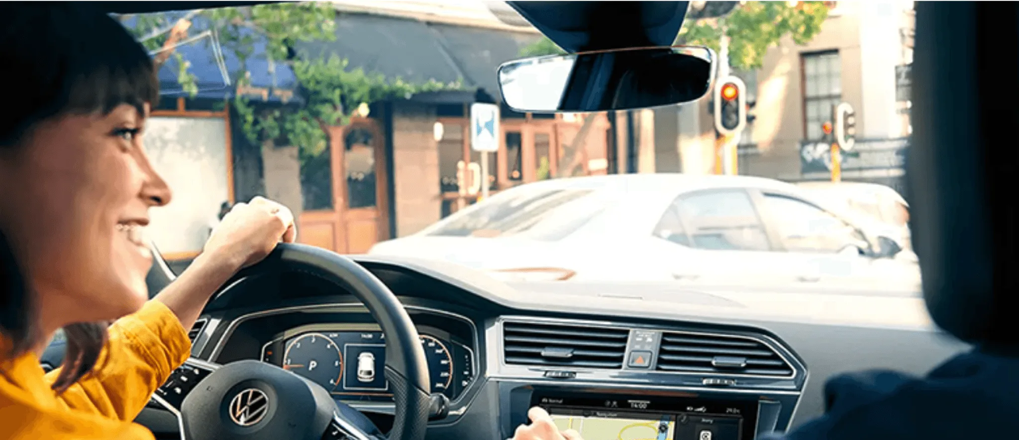 Smiling woman driving a Volkswagen through a city street, with the digital dashboard and touchscreen navigation in view