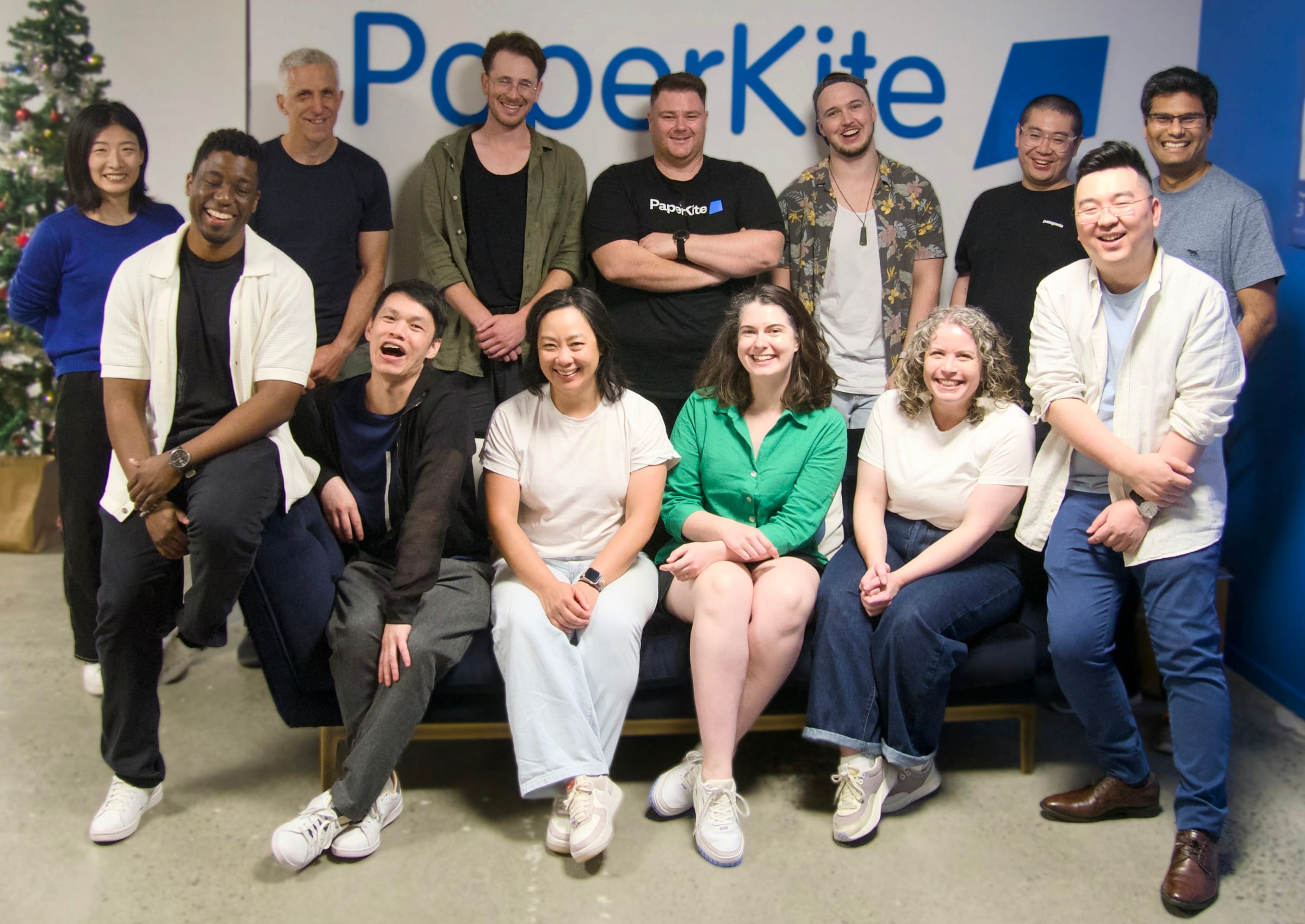 A group photo of the PaperKite team standing together in front of a PaperKite sign, smiling and celebrating teamwork